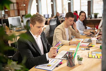 Image showing Young caucasian colleagues working together in a office using modern devices and gadgets