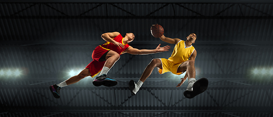 Image showing Young basketball players in competitive fight, motion in flight on black background, look from the bottom. Concept of sport, movement, energy and dynamic.