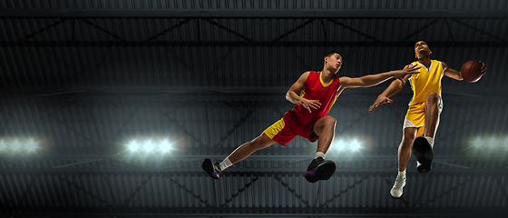 Image showing Young basketball players in competitive fight, motion in flight on black background, look from the bottom. Concept of sport, movement, energy and dynamic.