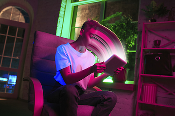 Image showing Cinematic portrait of stylish woman in neon lighted interior using a tablet. The face is smeared, sucked into the screen. The concept of social network dependency