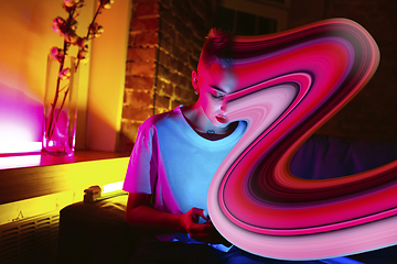 Image showing Cinematic portrait of stylish woman in neon lighted interior using a smartphone. The face is smeared, sucked into the phone. The concept of social network dependency