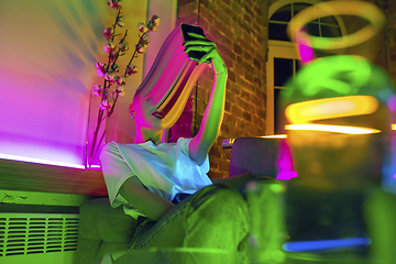 Image showing Cinematic portrait of stylish woman in neon lighted interior using a smartphone. The face is smeared, sucked into the phone. The concept of social network dependency