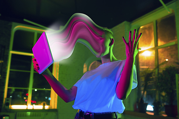 Image showing Cinematic portrait of stylish woman in neon lighted interior using a tablet. The face is smeared, sucked into the screen. The concept of social network dependency