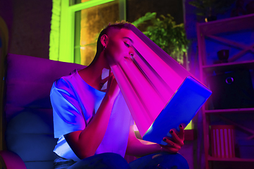 Image showing Cinematic portrait of stylish woman in neon lighted interior using a tablet. The face is smeared, sucked into the screen. The concept of social network dependency