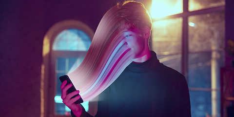 Image showing Cinematic portrait of stylish man in neon lighted interior using a smartphone. The face is smeared, sucked into the phone. The concept of social network dependency