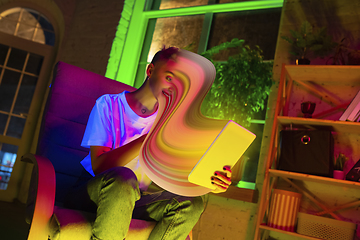 Image showing Cinematic portrait of stylish woman in neon lighted interior using a tablet. The face is smeared, sucked into the screen. The concept of social network dependency