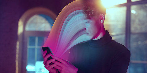 Image showing Cinematic portrait of stylish man in neon lighted interior using a smartphone. The face is smeared, sucked into the screen. The concept of social network dependency