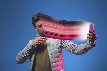 Image showing Cinematic portrait of stylish man in neon lighted interior using a smartphone. The face is smeared, sucked into the phone. The concept of social network dependency