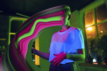 Image showing Cinematic portrait of stylish woman in neon lighted interior using a smartphone. The face is smeared, sucked into the phone. The concept of social network dependency
