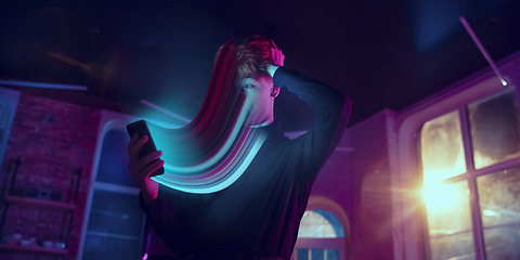 Image showing Cinematic portrait of stylish man in neon lighted interior using a smartphone. The face is smeared, sucked into the phone. The concept of social network dependency