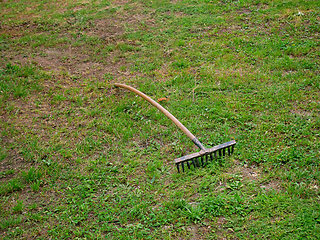 Image showing Old vintage rusty metal rake with a wooden handle on the ground 