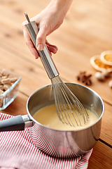 Image showing close up of hand with whisk stirring eggnog in pot
