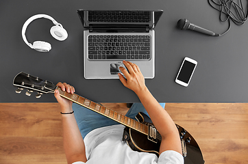 Image showing young man with laptop playing guitar at table