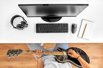 Image showing young man with computer playing guitar at table