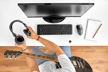 Image showing young man with headphones and guitar at table