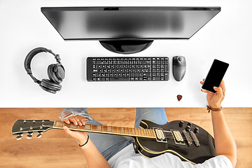 Image showing young man with guitar and smartphone at table