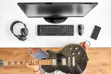 Image showing young man with computer tuning guitar at table