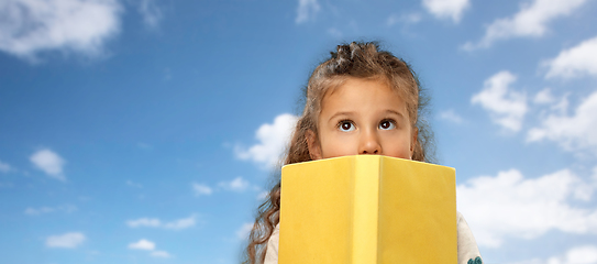 Image showing little girl hiding behind book over sky and clouds