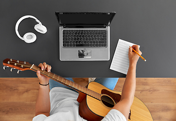 Image showing man with guitar writing to music book at table