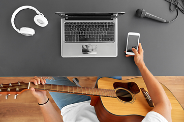 Image showing young man with guitar and smartphone at table