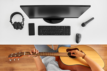 Image showing young man with computer playing guitar at table