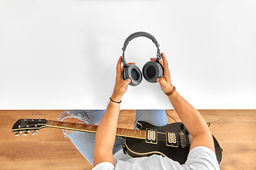 Image showing young man with headphones and guitar at table