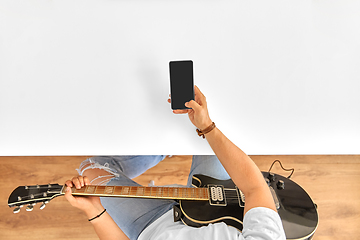 Image showing young man with guitar and smartphone at table