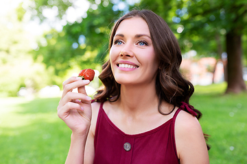 Image showing happy woman eating strawberry at summer park