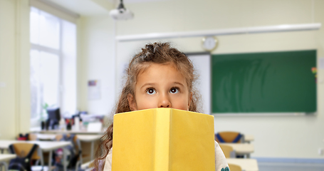 Image showing little girl hiding behind yellow book at school