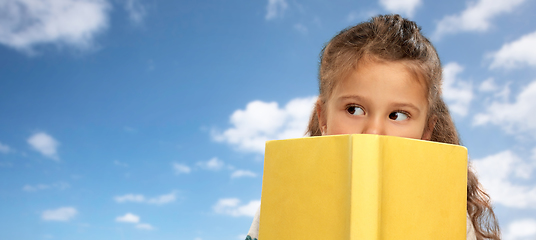 Image showing little girl hiding behind book over sky and clouds