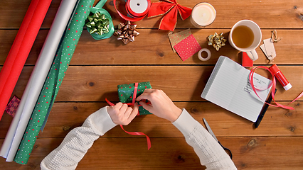 Image showing hands packing christmas gift and tying ribbon