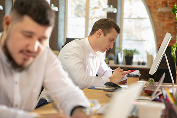 Image showing Young caucasian colleagues working together in a office using modern devices and gadgets