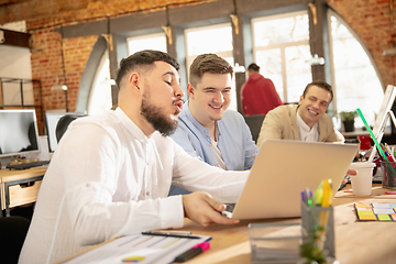 Image showing Young caucasian colleagues working together in a office using modern devices and gadgets