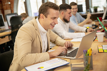 Image showing Young caucasian colleagues working together in a office using modern devices and gadgets