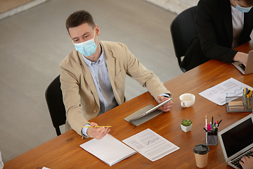 Image showing High angle view colleagues working together in face masks during quarantine in a office using modern devices and gadgets during creative meeting