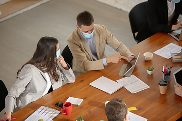 Image showing High angle view colleagues working together in face masks during quarantine in a office using modern devices and gadgets during creative meeting