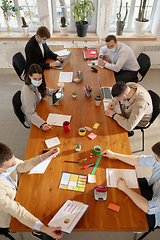 Image showing High angle view colleagues working together in face masks during quarantine in a office using modern devices and gadgets during creative meeting