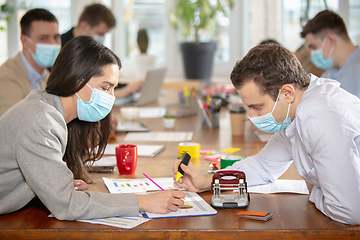 Image showing Side view colleagues working together in face masks during quarantine in a office using modern devices and gadgets during creative meeting