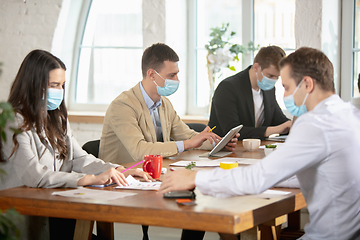 Image showing Side view colleagues working together in face masks during quarantine in a office using modern devices and gadgets during creative meeting