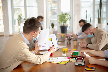 Image showing Side view colleagues working together in face masks during quarantine in a office using modern devices and gadgets during creative meeting