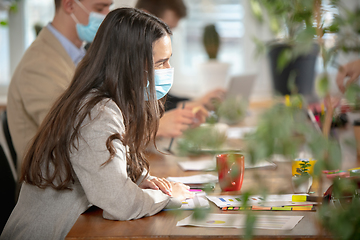 Image showing Side view colleagues working together in face masks during quarantine in a office using modern devices and gadgets during creative meeting