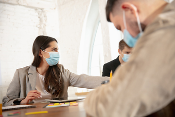 Image showing Side view colleagues working together in face masks during quarantine in a office using modern devices and gadgets during creative meeting