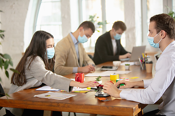 Image showing Side view colleagues working together in face masks during quarantine in a office using modern devices and gadgets during creative meeting