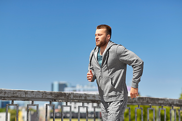 Image showing happy young man running across city bridge