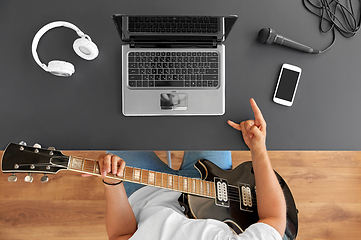 Image showing young man with laptop playing guitar at table