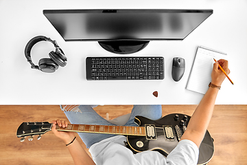 Image showing man with guitar writing to music book at table