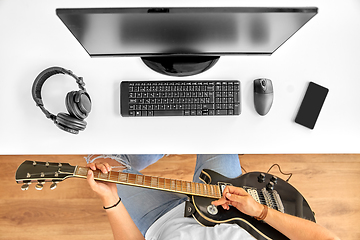 Image showing young man with computer playing guitar at table