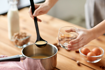 Image showing hands with ladle pouring eggnog from pot to glass