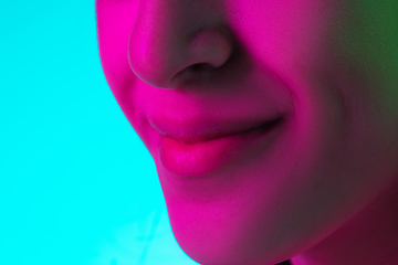 Image showing Close up beautiful woman\'s smile isolated on blue studio background in multicolored neon light