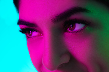Image showing Close up beautiful woman\'s eyes isolated on blue studio background in multicolored neon light
